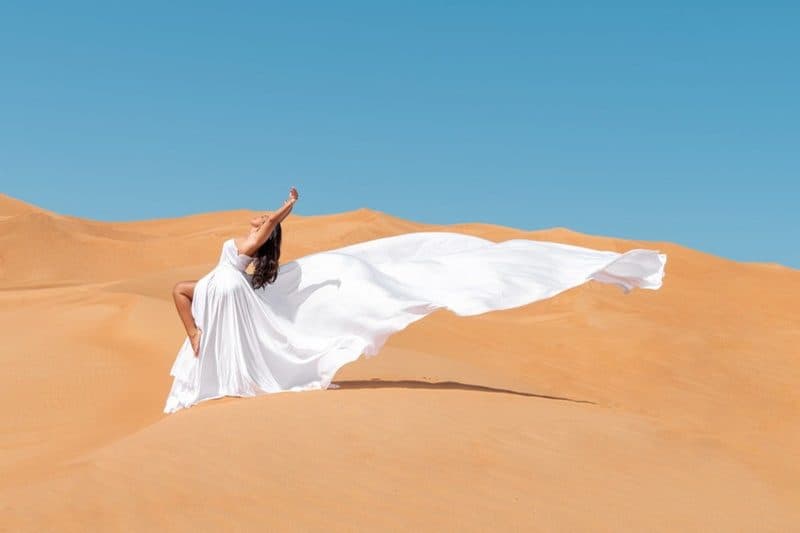 A flying-dress photoshoot in a white gown on a desert dune