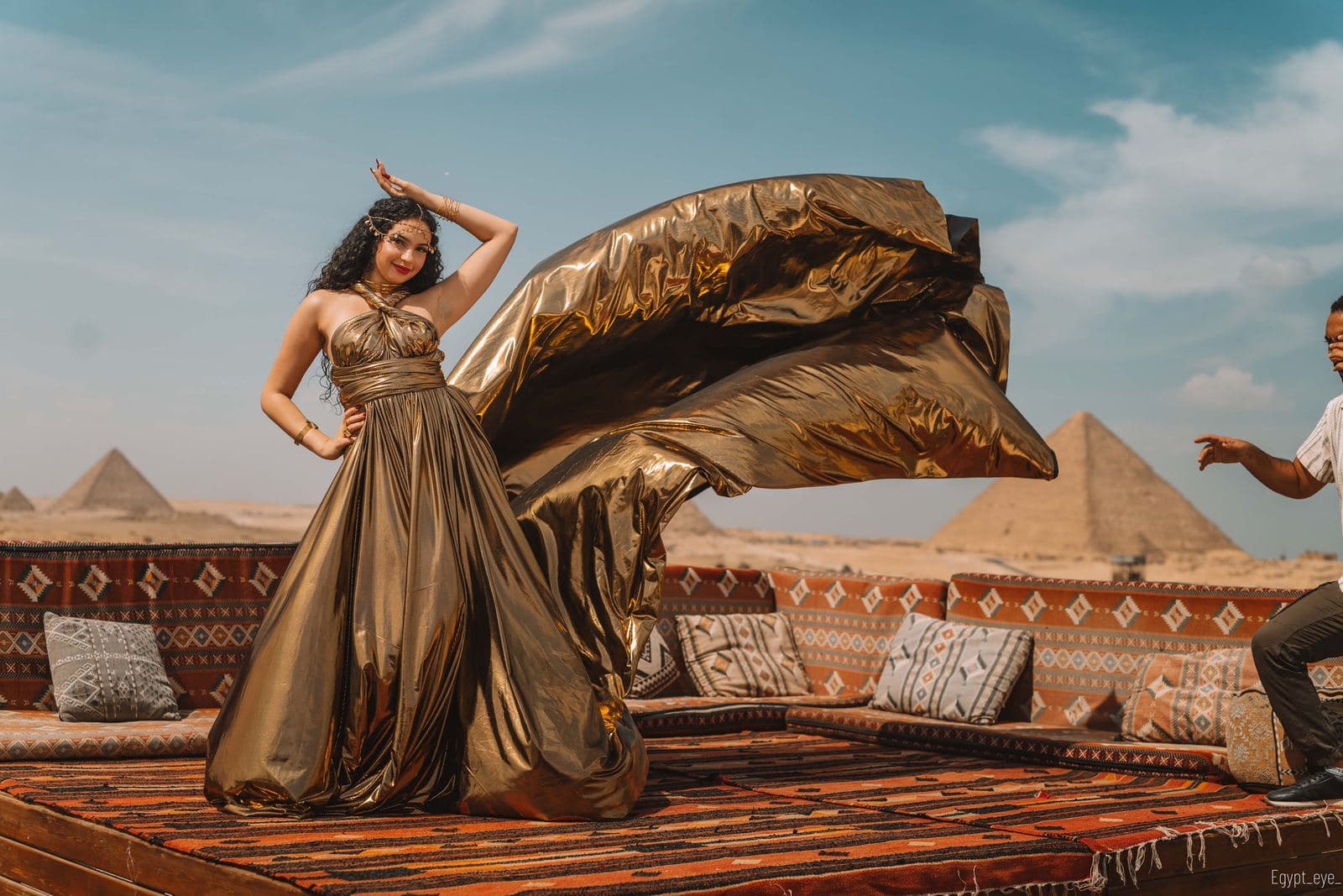 The assistant at the right of frame, mid-throw, sending the gold train up into the air behind the wearer