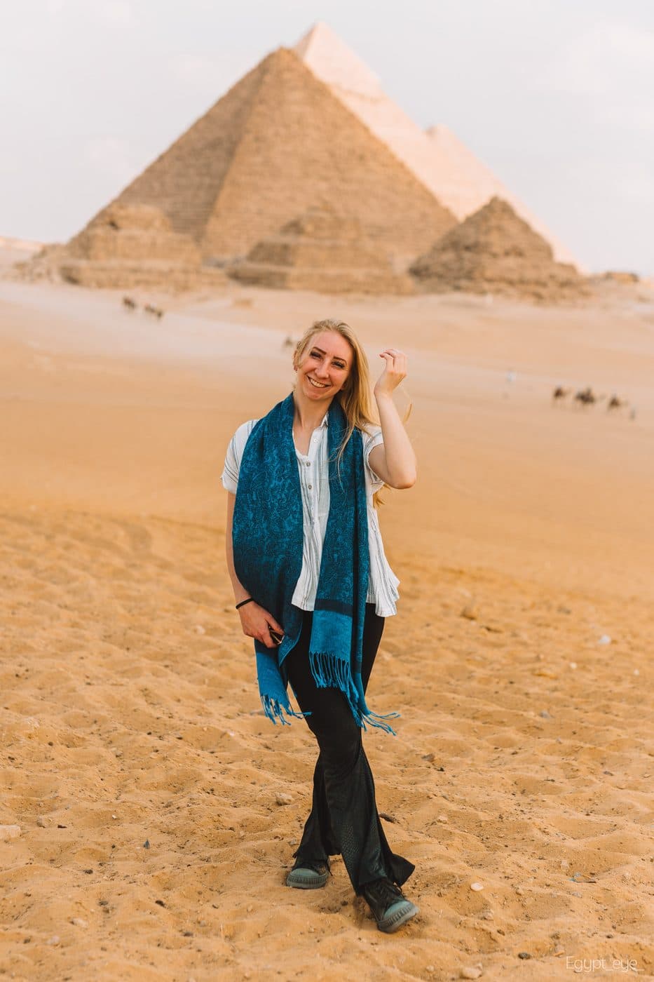 A visitor standing on the sand at Giza in warm afternoon light, two pyramids filling the frame behind her