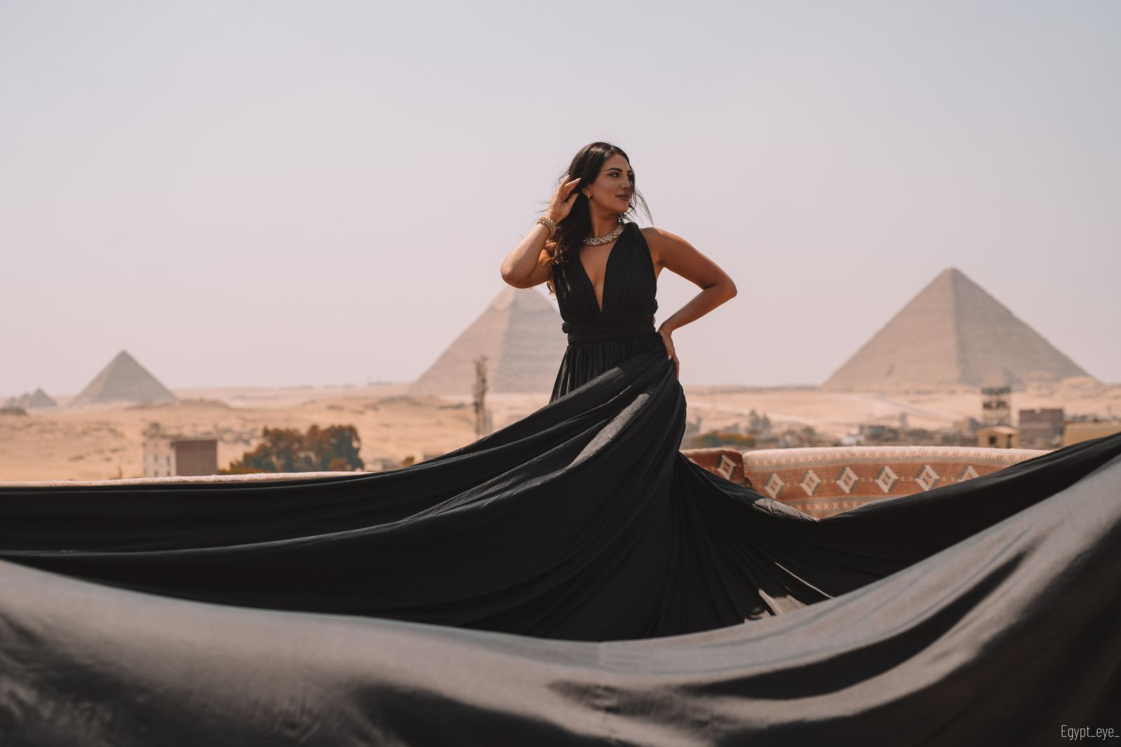 The Black dress on the rooftop, its train laid out long and low with the pyramids behind