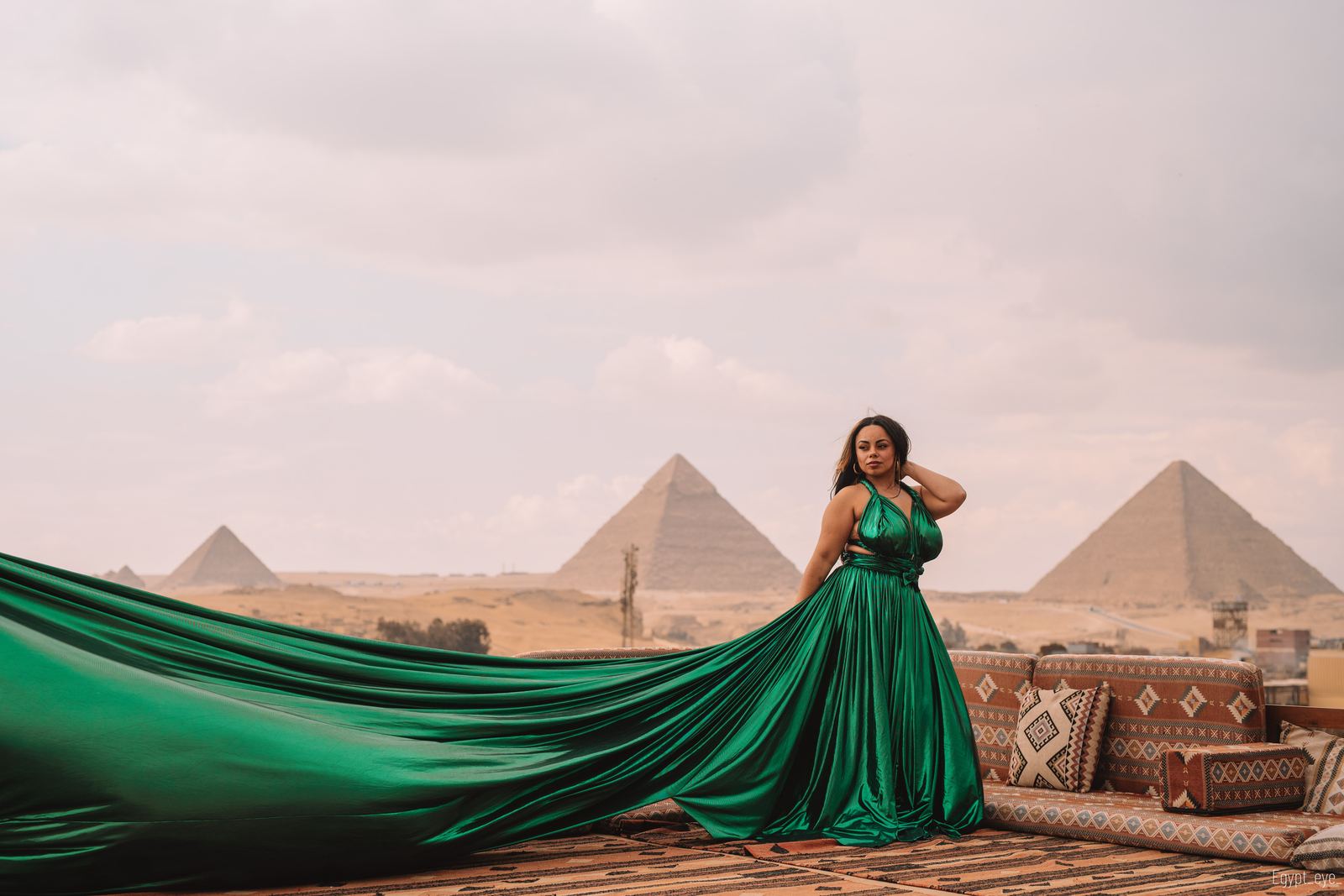 The Emerald dress on the rooftop, deep green silk running out across the terrace toward the pyramids
