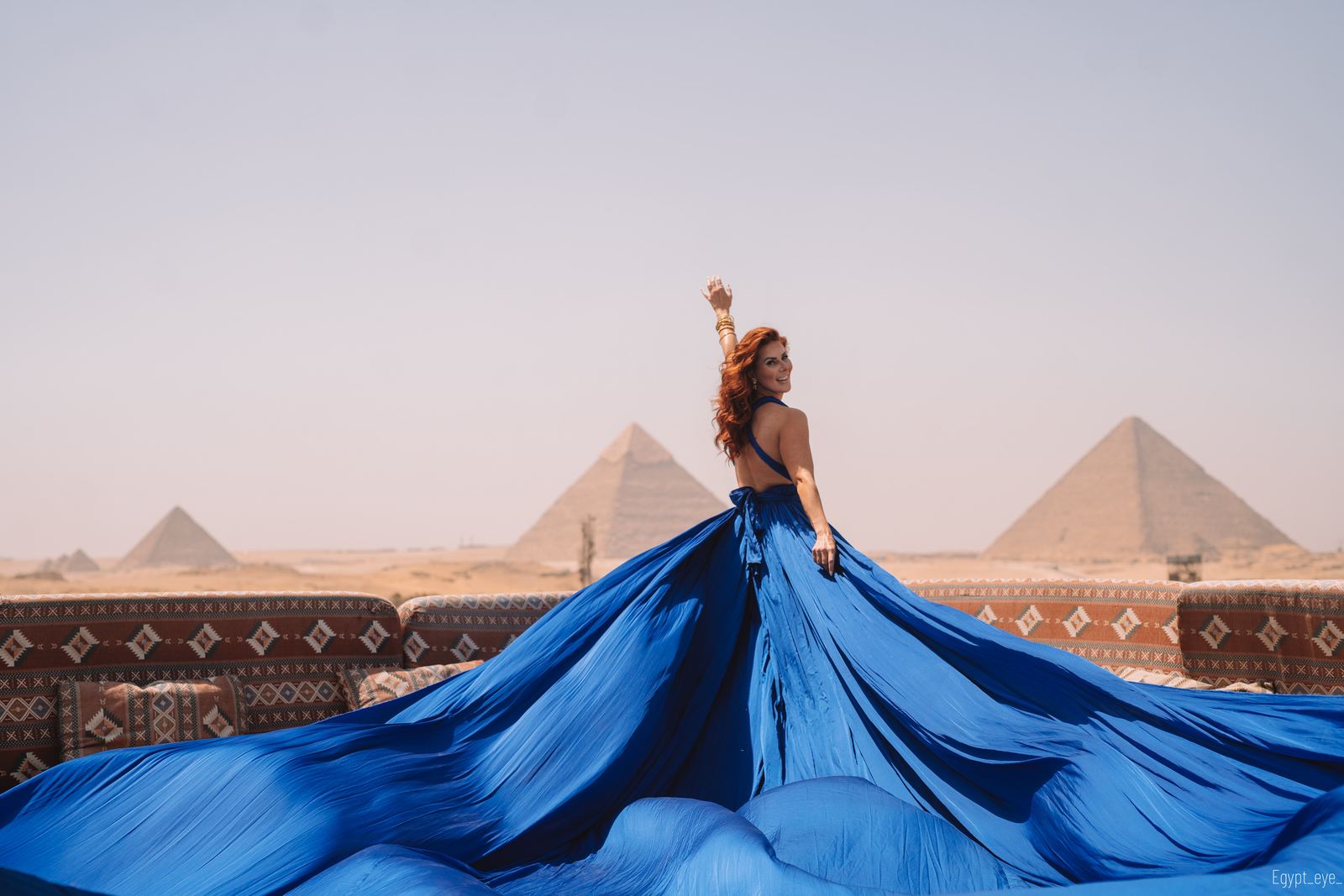 The Navy dress spread into a wide circle on the rooftop, arm raised, three pyramids on the skyline