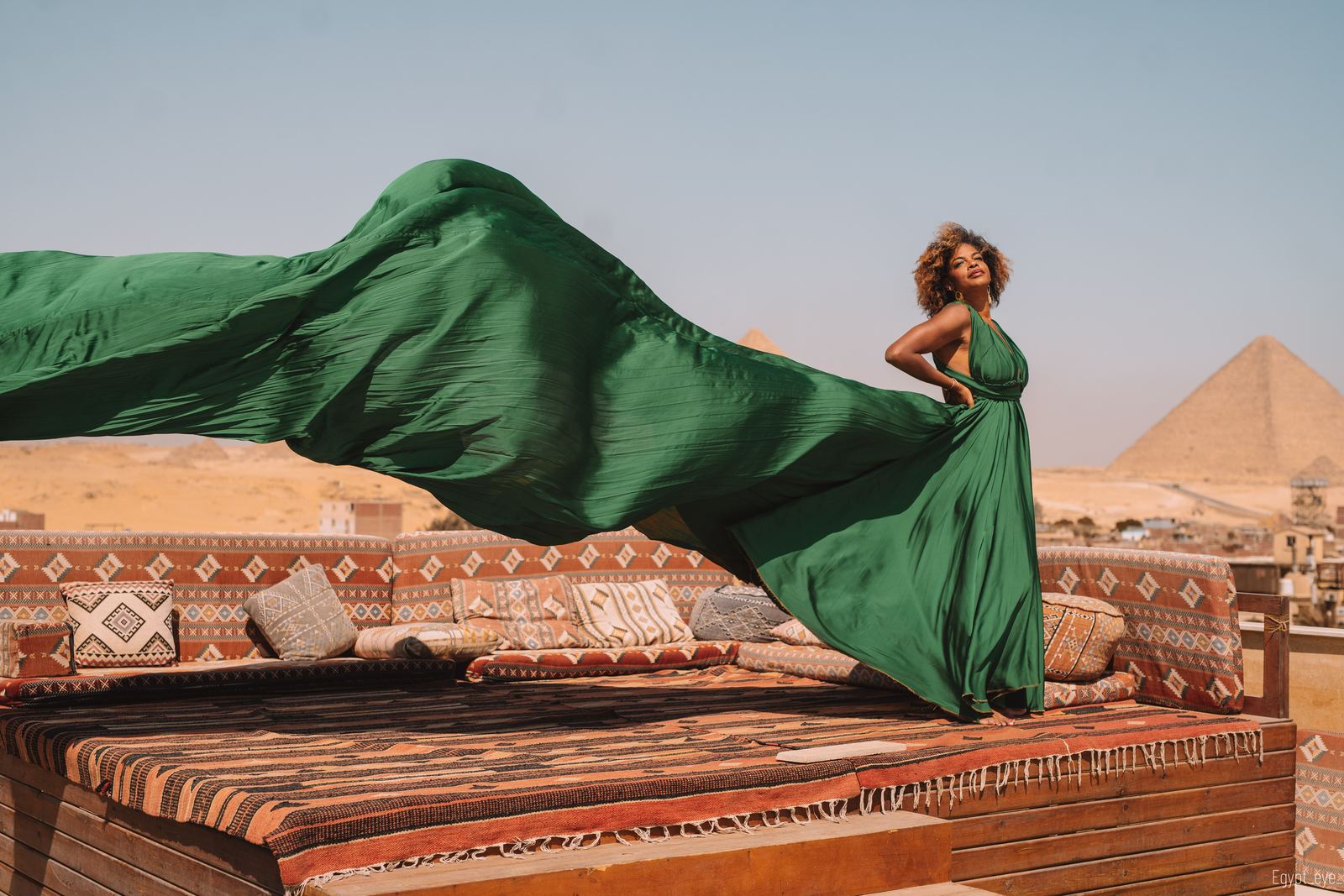 The Verdant dress caught mid-air, green fabric arcing across the rooftop toward the pyramids